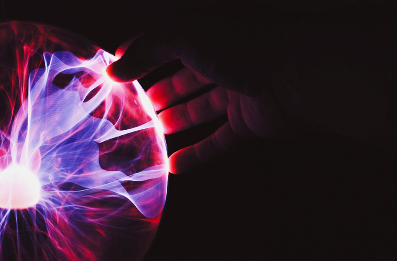 A hand touching a plasma globe